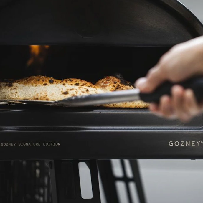 gozney-roccbox-schwarz-in-betrieb,-eine-pizza-wird-geraden-aus-dem-ofen-genommen.